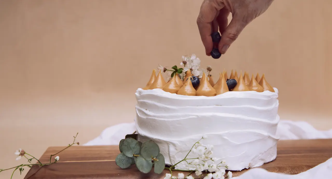 Torta blanca con merengues de caramelo y arándanos, decorada con flores y eucalipto